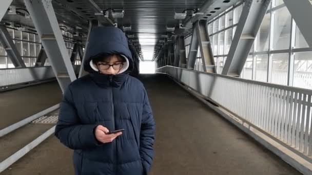 Un hombre solitario con una chaqueta de invierno camina a través de un cruce peatonal de metal . — Vídeo de stock