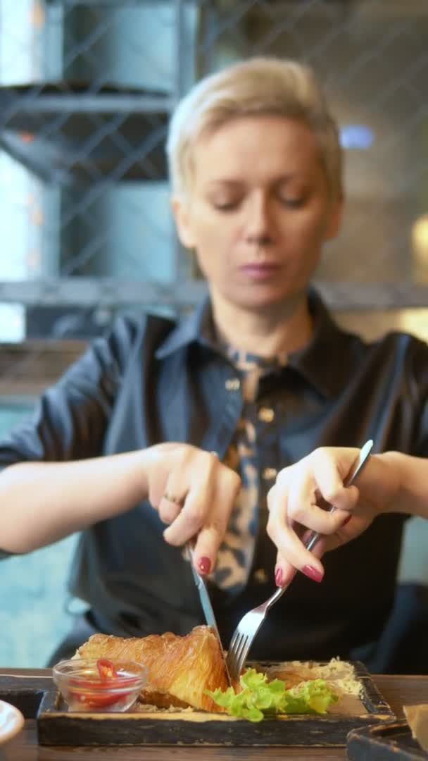 Närbild. kvinna äter en croissant med bacon och kaffe i ett café. vertikalt skott — Stockvideo