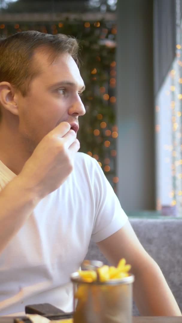 Verticaal schot. man eet broodje met spek en friet in het restaurant. — Stockvideo