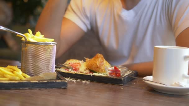 Yakın plan. Adam restoranda pastırmalı sandviç ve patates kızartması yiyor.. — Stok video
