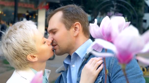 Hermosa pareja enamorada, hombre y mujer beso entre las flores rosa Magnolia — Vídeo de stock