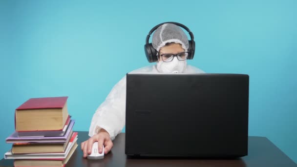 Een man met een beschermend masker en pak gebruikt een laptop en boeken. blauwe achtergrond — Stockvideo