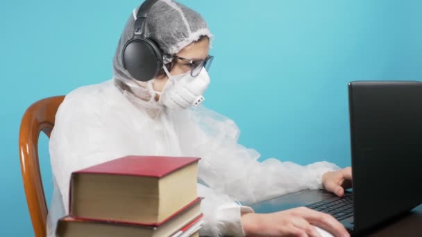 Koruyucu maskeli ve takım elbiseli bir adam dizüstü bilgisayar ve kitap kullanıyor. mavi arkaplan — Stok video
