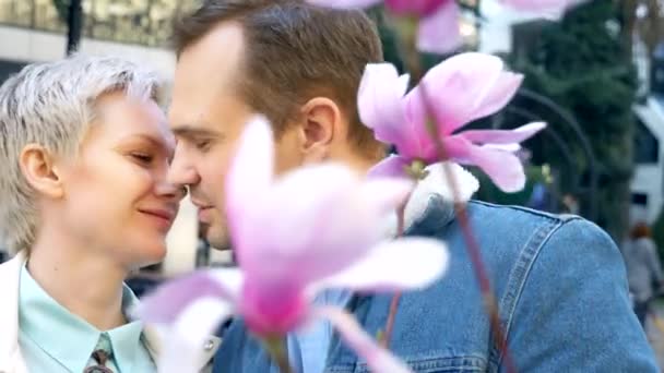 Vacker par kär, man och kvinna kyss bland blommorna rosa Magnolia — Stockvideo