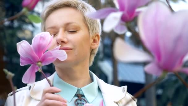 Portrait de belle blonde élégante aux cheveux courts parmi les fleurs roses de Magnolia — Video