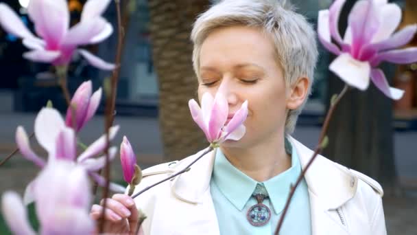Portrait of beautiful stylish blonde with short hair among pink Magnolia flower — Stock Video