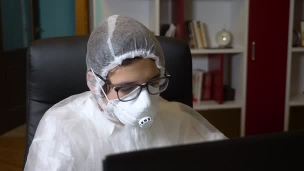 De man in ademhalingsapparaat en beschermend pak met behulp van zijn laptop terwijl thuis zitten — Stockvideo