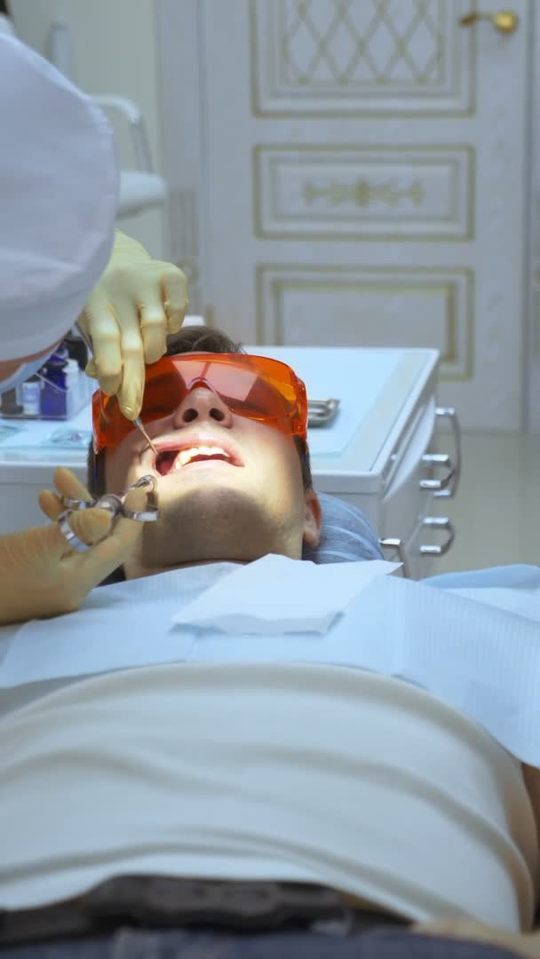 Tiro vertical. o dentista trata o homem bonito dente . — Vídeo de Stock
