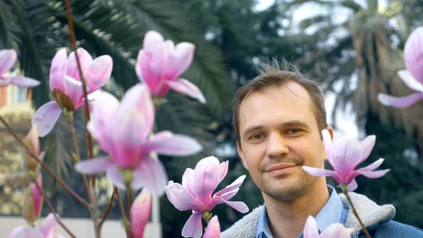 Portret młodego przystojnego mężczyzny wśród różowego kwiatu Magnolii — Zdjęcie stockowe