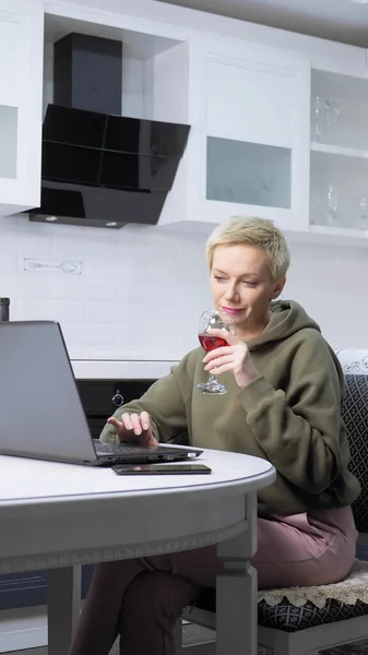 Pionowy strzał. stylowa kobieta używa laptopa i pije wino w kuchni — Zdjęcie stockowe