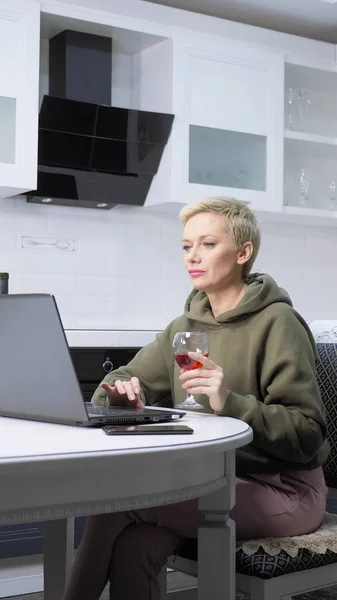 Pionowy strzał. stylowa kobieta używa laptopa i pije wino w kuchni — Zdjęcie stockowe