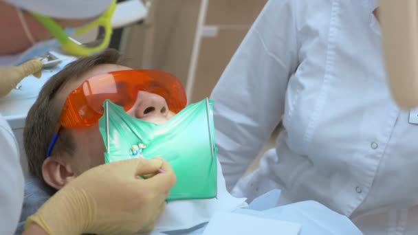Nahaufnahme. Zahnarzt behandelt Zahn männlichen Patienten. Sofferdam nutzen — Stockvideo