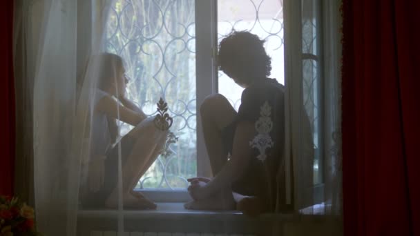 Tonårsbror och tonårssyster sitter på fönsterbrädan bakom tyll. — Stockvideo