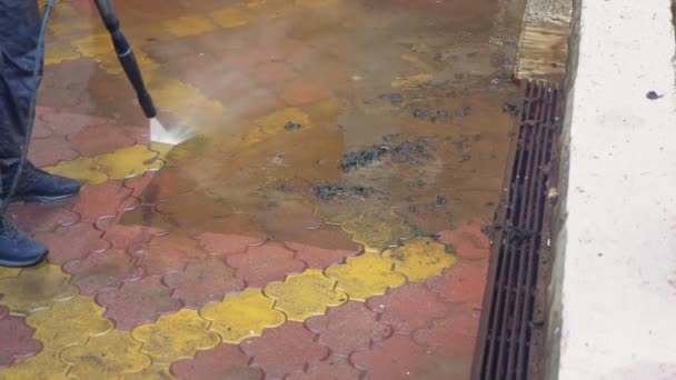 A man cleans the tile on the sidewalk from the build up of dirt. — Stock Video