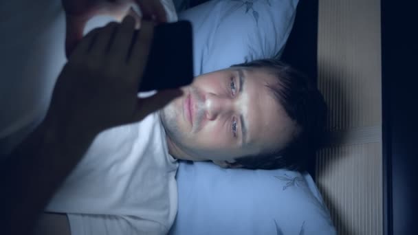 Tiro vertical de um jovem usa um smartphone na cama à noite — Vídeo de Stock