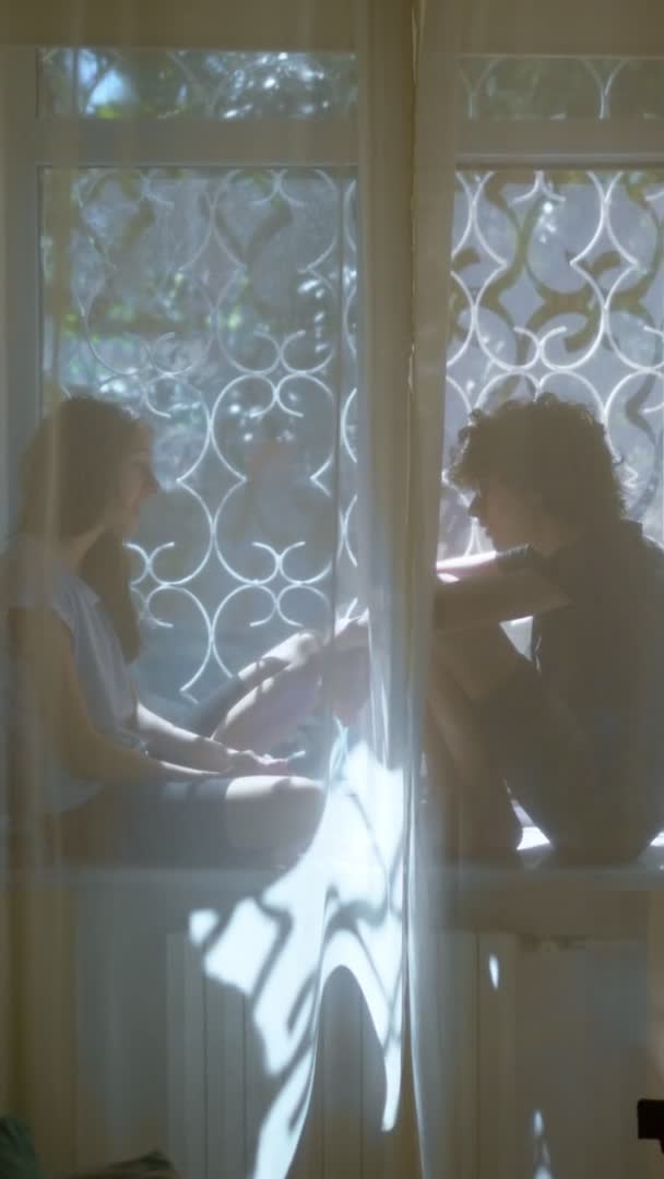 Verticalmente, hermano adolescente y hermana están sentados en el alféizar de la ventana — Vídeos de Stock