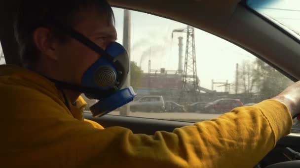 Mężczyzna w respiratorze jeździ samochodem obok palących kominów fabryki. — Wideo stockowe