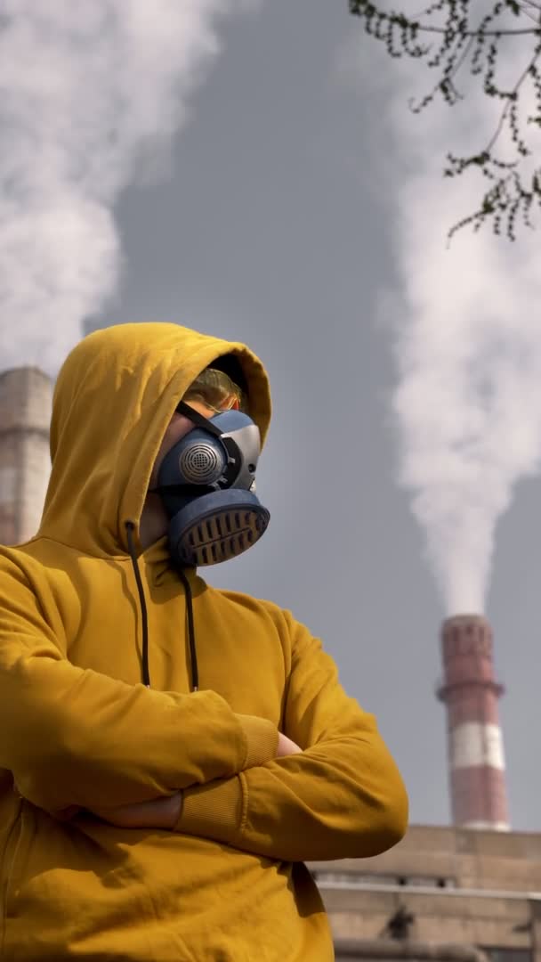 Κατακόρυφα. Ένας άντρας με αναπνευστήρα στέκεται απέναντι σε μια καμινάδα εργοστασίου καπνίσματος. — Αρχείο Βίντεο