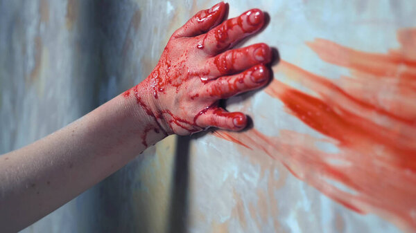 a female hand reaches out, holding on to the wall, leaving a trace of blood
