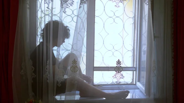 Adolescente menino senta-se no peitoril da janela atrás do tule em odinochestve . — Fotografia de Stock