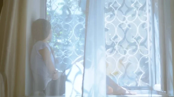 Дівчина-підліток сидить на підвіконні і дивиться у вікно. розмивання . — стокове фото