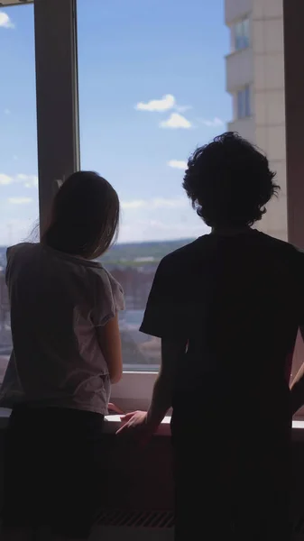 Verticalmente. siluetas. hermano y hermana Adolescentes miran por la ventana —  Fotos de Stock