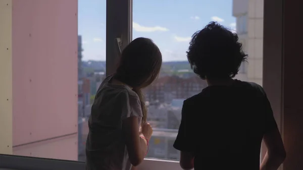 Sylwetki. brat i siostra nastolatki patrzeć przez okno — Zdjęcie stockowe