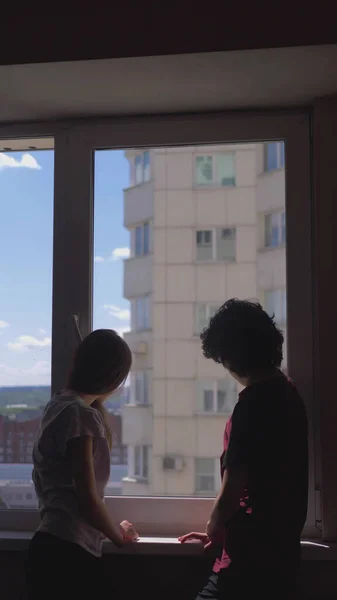 Verticaal. silhouetten. broer en zus tieners kijken uit het raam — Stockfoto