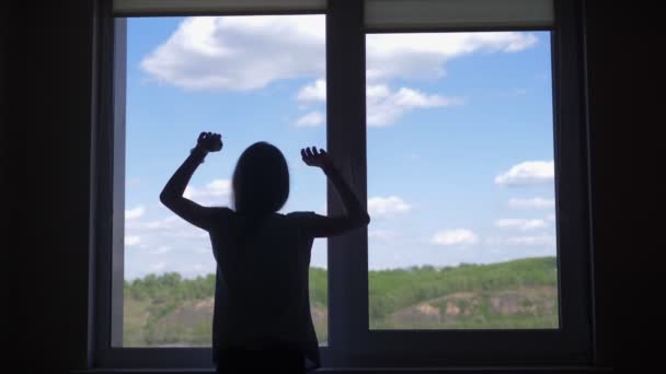 Sylwetka. dziewczyna jest rozciągnięty przez okno z widokiem na niebo i góry — Wideo stockowe