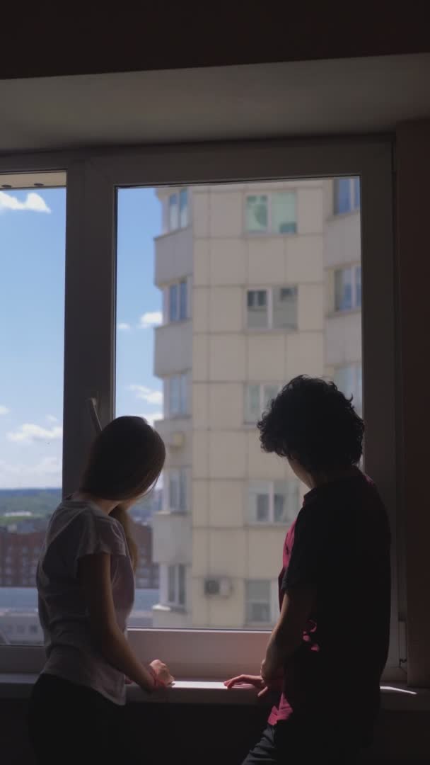 Verticalmente. siluetas. hermano y hermana Adolescentes miran por la ventana — Vídeos de Stock