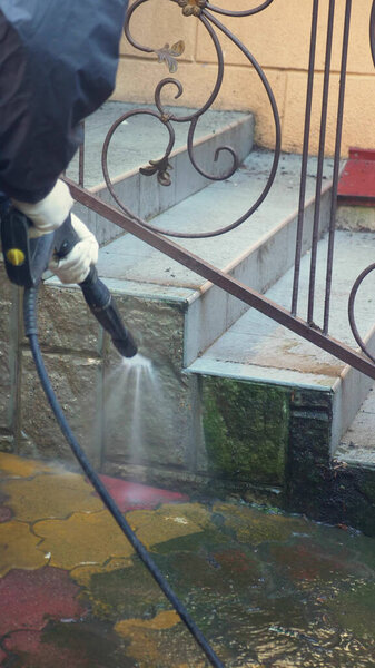 мужчина очищает плитку на тротуаре от грязи. вертикально
