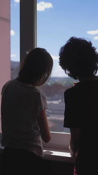 Vertikal. Silhouetten. Bruder und Schwester Teenager schauen aus dem Fenster — Stockfoto