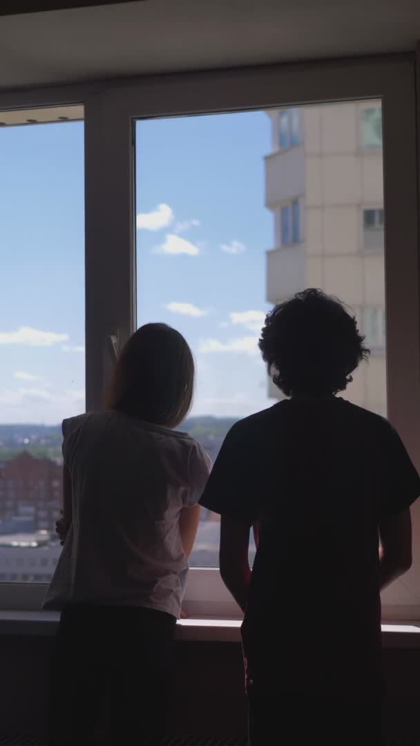 Вертикально. Силуэты. брат и сестра Подростки смотрят в окно — стоковое видео