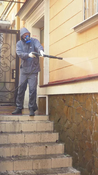 Verticalmente. Un hombre en la máscara está limpiando una casa afuera con una lavadora de alta presión — Foto de Stock