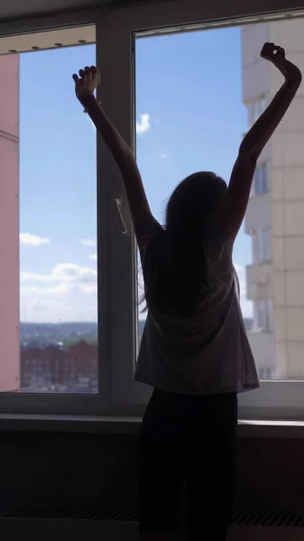 Verticalmente. silueta. chica se estira por la ventana con una vista del cielo —  Fotos de Stock