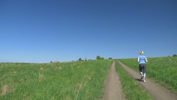 Струнка жінка біжить в полі на пагорбах, вид ззаду — стокове відео