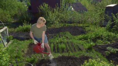 Bahçedeki toprağı kırmızı sulama tenekesinden sulayan güzel genç bir kadın.