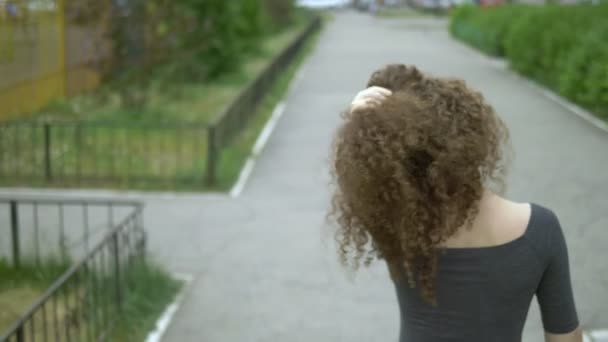 Vista trasera. mujer con el pelo rizado toca su cabello de pie en una calle de la ciudad — Vídeo de stock