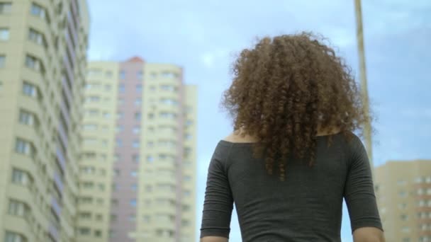 Vista para trás. mulher com cabelo encaracolado caminha ao longo de uma rua da cidade, o vento em seu cabelo — Vídeo de Stock