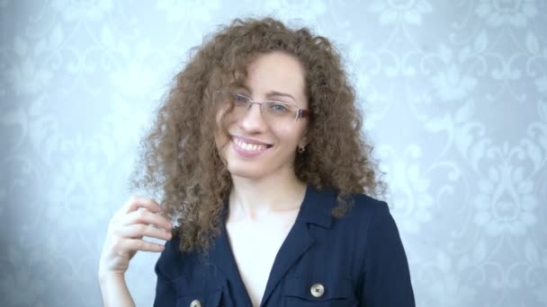 Retrato. Hermosa mujer sonriente en gafas con el pelo rizado toca su cabello — Vídeo de stock