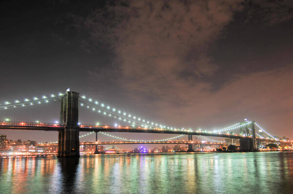 Brooklyn Bridge closeup over East River at night in New York City Manhattan with lights and reflections.