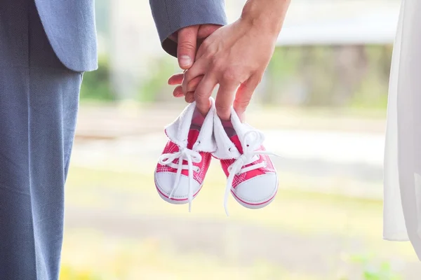 En bild av vuxna håller baby par sneakers i rött. Graviditet och förväntan. — Stockfoto