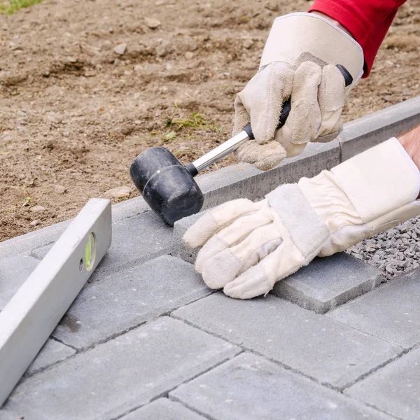 Murarz umieszcza bloków betonowych brukowych do budowania utorować patio, za pomocą młotka i poziomicy. Złota rączka Diy koncepcja — Zdjęcie stockowe