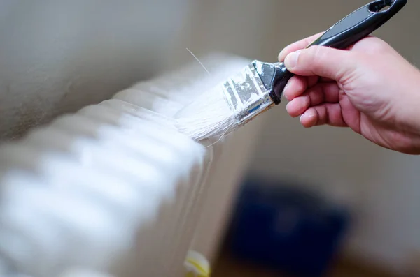 Närbild av målare arm målning en värme radiator med paint roller. Professional Workman handen håller smutsiga pensel. — Stockfoto