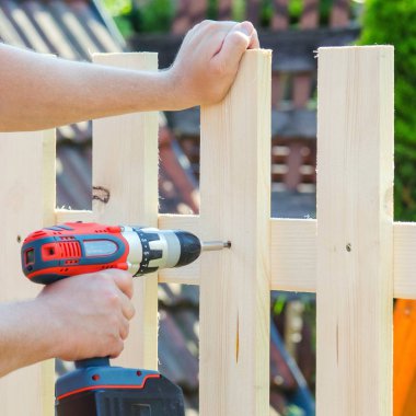 Adam Bina ahşap çit bir matkap ve vida ile eller. DIY kavramı. Onun el ve aracı kapat.   