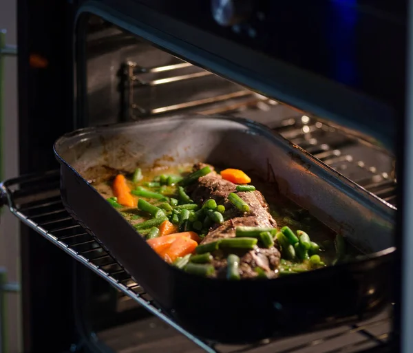 烤的肉 vith 豌豆和胡萝卜在烤箱. — 图库照片