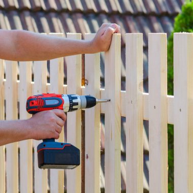Adam Bina ahşap çit bir matkap ve vida ile eller. DIY kavramı. Onun el ve aracı kapat.   