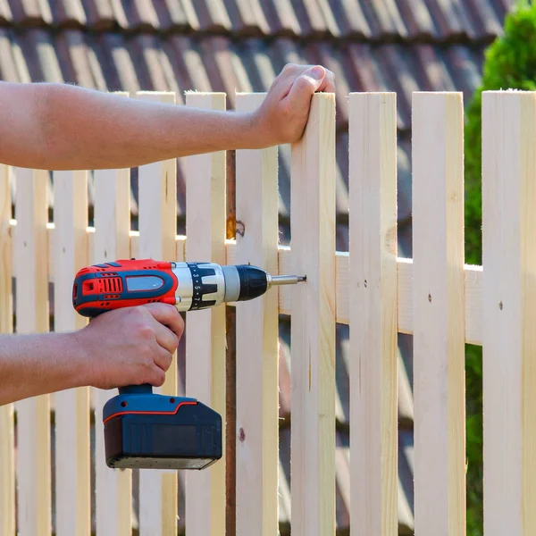 Adam Bina ahşap çit bir matkap ve vida ile eller. DIY kavramı. Onun el ve aracı kapat.   