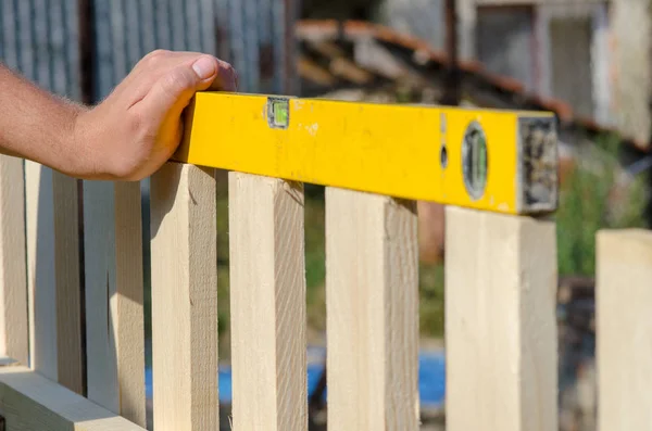 Man een houten hek bouwen en controleren met de waterpas. Close up van zijn hand en gereedschap. — Stockfoto