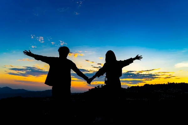 在蓝天的高山上 年轻的亚洲夫妻牵着手的轮廓 享受和平时刻的概念 爱的家庭关系概念 图库照片